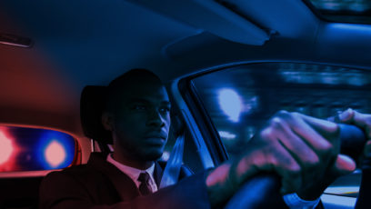 黑人坐在汽车的方向盘后面，红灯和蓝灯