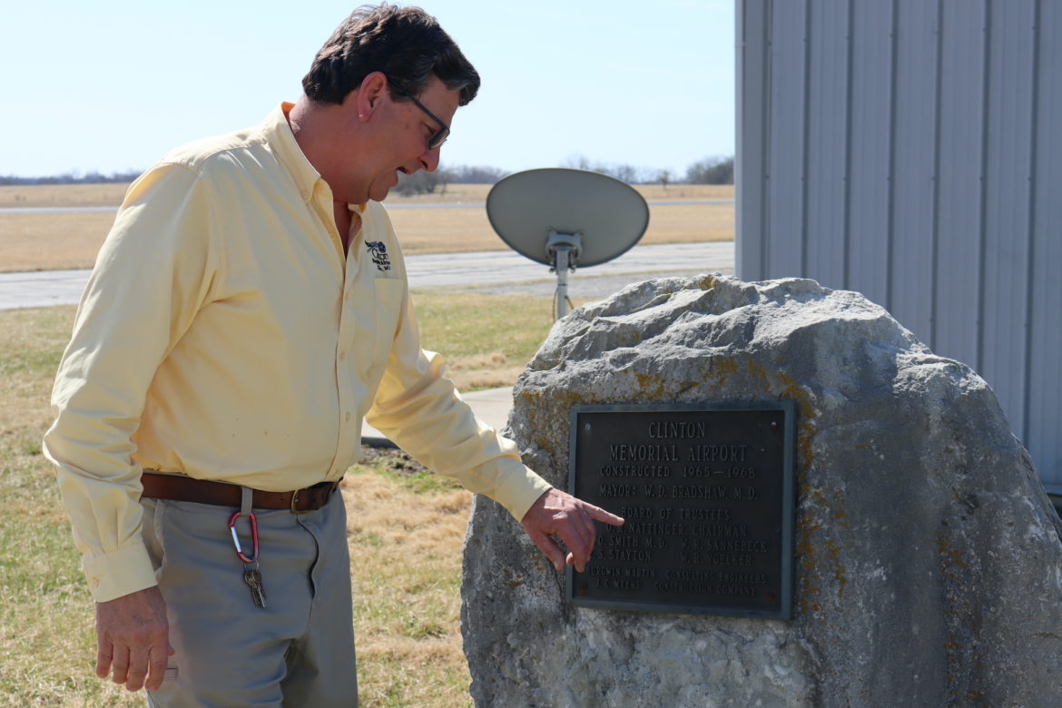 身穿黄色衬衫的男子指着一座纪念机场创始人的岩石纪念碑。