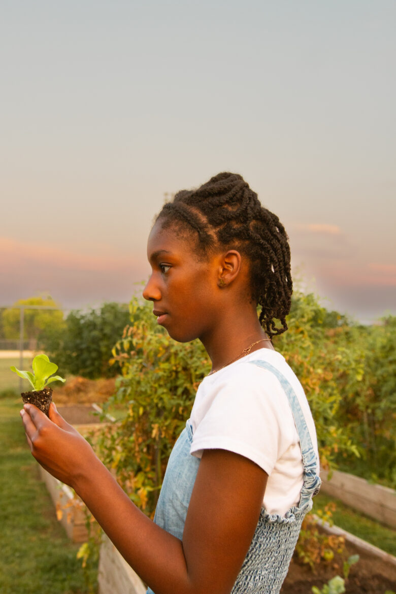夕阳西下时，年轻的黑人女孩扎拉·巴(Zara Ba)手里拿着她的莴苣，站在堪萨斯城天空下的高床之间。纪stribling摄于《平地》